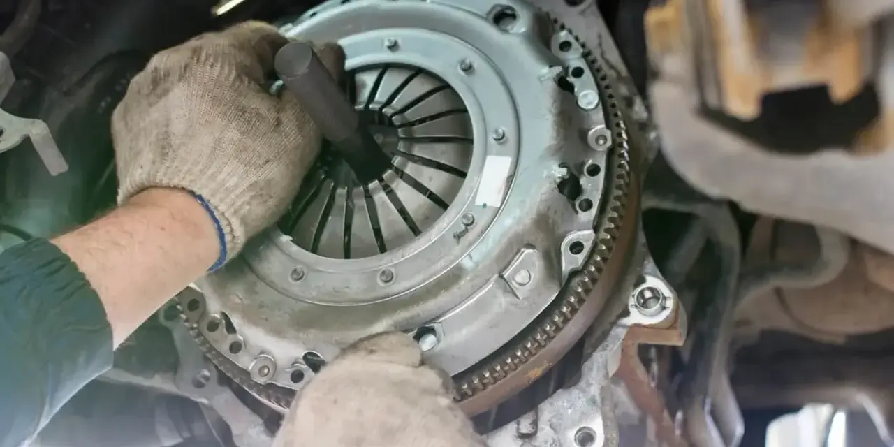 Mechanik w rękawiczkach montuje nowe sprzęgło w samochodzie. Widać jego dłonie i narzędzie, gdzie jest sprzęgło.