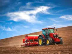 Czerwony traktor z siewnikiem na polu. Zastanawiasz się, jaki podatek od zakupu ciągnika rolniczego?