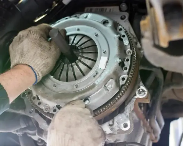 Mechanik w rękawiczkach montuje nowe sprzęgło w samochodzie. Widać jego dłonie i narzędzie, gdzie jest sprzęgło.