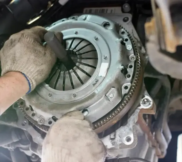 Mechanik w rękawiczkach montuje nowe sprzęgło w samochodzie. Widać jego dłonie i narzędzie, gdzie jest sprzęgło.
