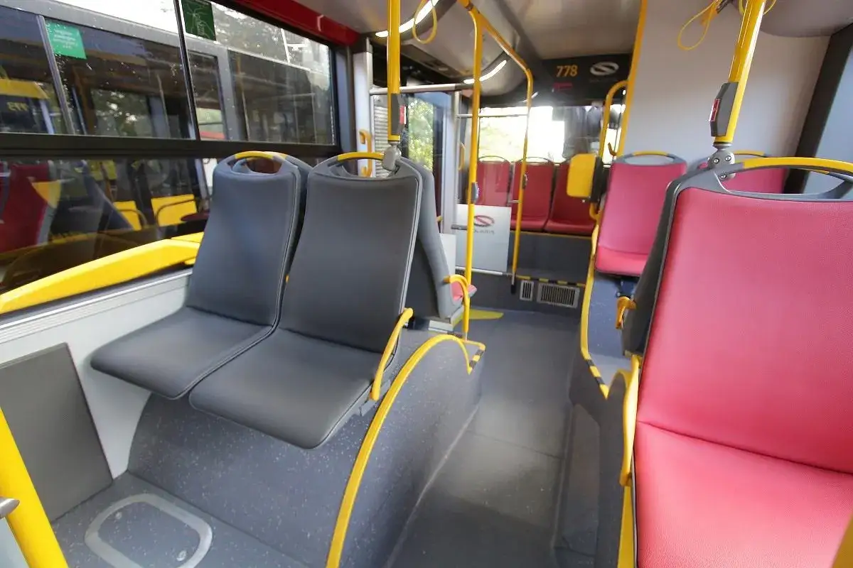 Wnętrze autobusu z szarymi i czerwonymi siedzeniami. Widać żółte poręcze i numer 778. Trudno ocenić, ile miejsc ma autokar.