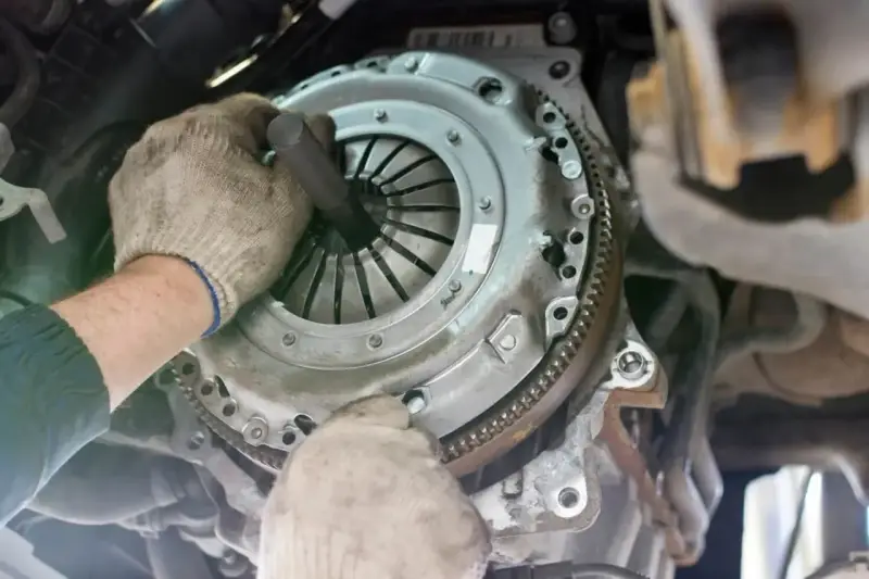 Mechanik w rękawiczkach montuje nowe sprzęgło w samochodzie. Widać jego dłonie i narzędzie, gdzie jest sprzęgło.